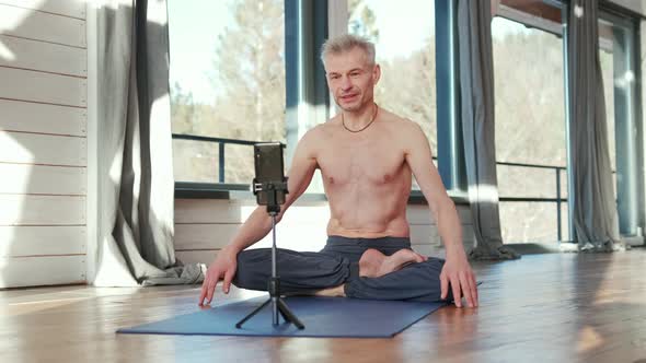 Yoga Man Sitting Cross Legged on the Floor Doing Online Workout in Front of the Phone