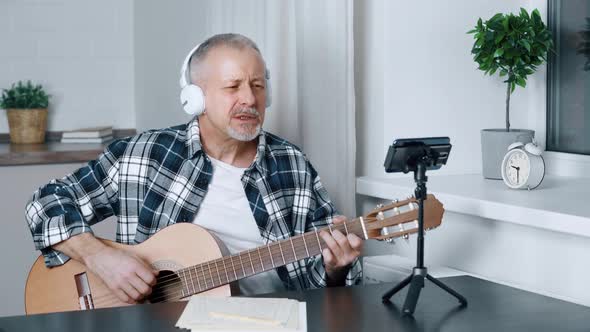 Smiling Middleaged Blogger Plays Guitar While Shooting Video on Smartphone
