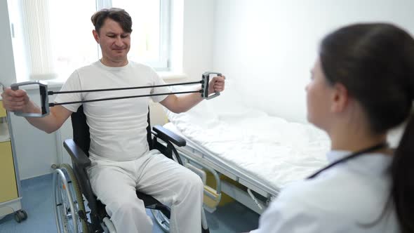 Weak Motivated Caucasian Man Exercising with Resistance Band Sitting in Wheelchair with Blurred