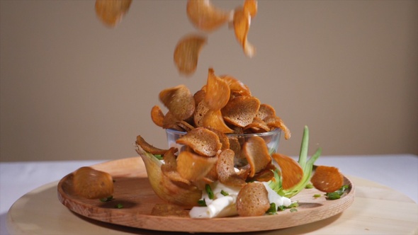 Tasty bread crackers falling on a wooden plate with onion in slow motion