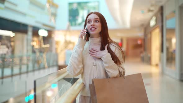 Portrait of Cheerful Young Woman Holding Shopping Paper Bags and Talking with Friend Using Modern