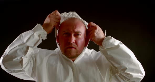 a Bald, Unshaven Man with a Serious and Focused Expression on Face Puts on a White Protective