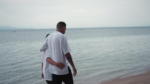 Married Gay Couple Men Walk By the Sea on a Beach During Honeymoon Trip  Back View