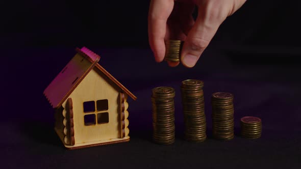 Small Wooden House with Columns of Coins on Black Background