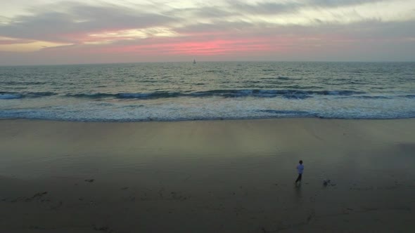 Aerial shot of little boy playing soccer on the beach at sunset.