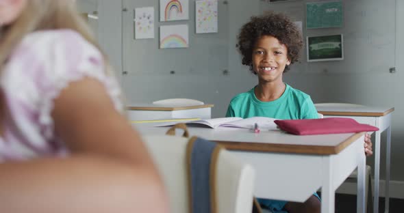 Video of happy biracial boy sitting at desk in classsroom alt