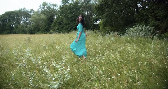 A Girl In A Long Dress Runs Across A Green Meadow 