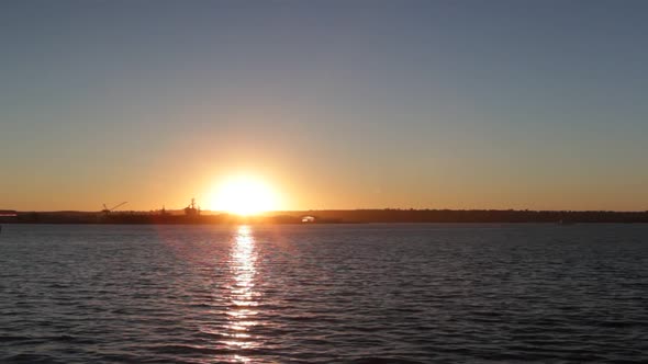 Sun Setting Over Water in Bay with Silhouette of Navy Ship and Reflection Wide