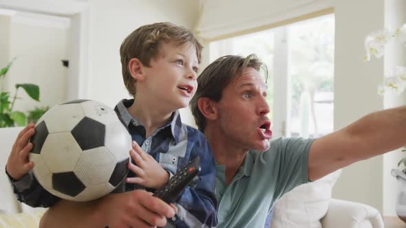 Happy caucasian father and son watching tv and supporting in living room