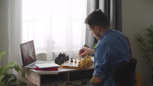 A Young Cute Man Plays Chess with a Different Video of a House During a Pandemic