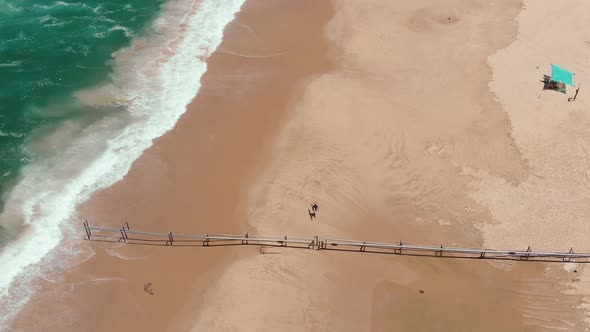 A lonely surfer walks on the beach while the wild endless sea crushing waves on the sand's coast lin