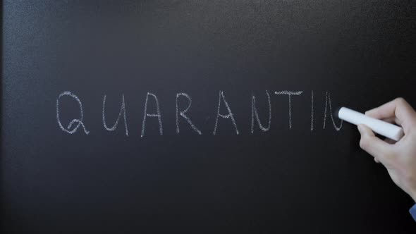 Hand writing word quarantine on chalkboard.