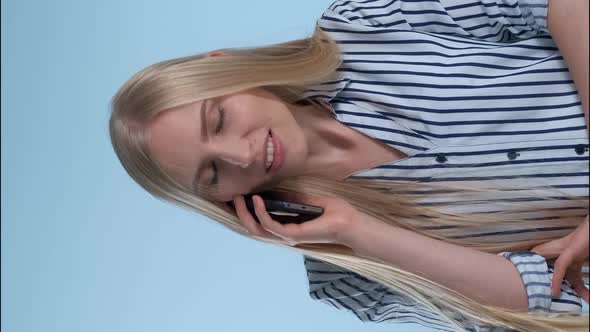 Pleasant-looking Young Lady Speaking with Somebody By Smartphone on Blue Background.