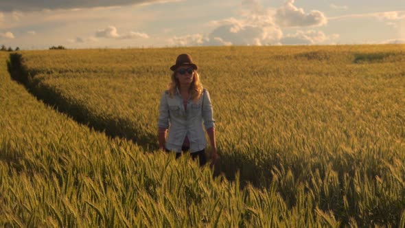 young caucasian bohemian female wearing hat in a  barley field during sunset
