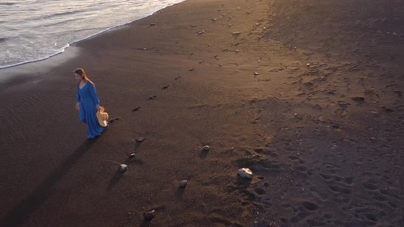 Aerial View of a Girl in a Blue Dress Walking on the Beach with Black Sand at Sunset. Tenerife