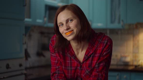 Young smiling 30s woman playing with orange peels in her mouth