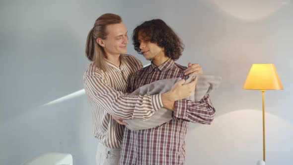 Smiling Young Gay Couple Hugging and Rocking Baby at Home