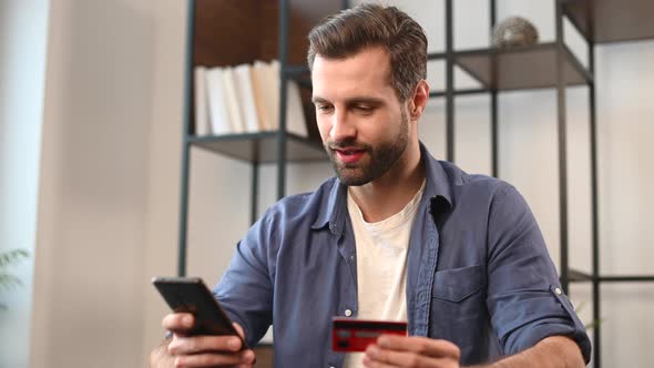 Young Bearded Hipster Guy in Casual Wear Using Mobile Phone and Credit Card