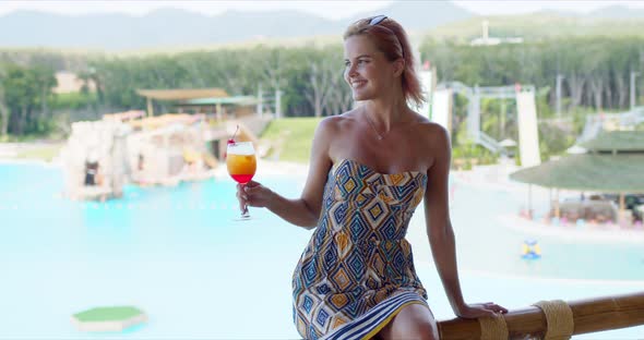 Happy Tourist with Fruit Beverage Sitting on Terrace Railing