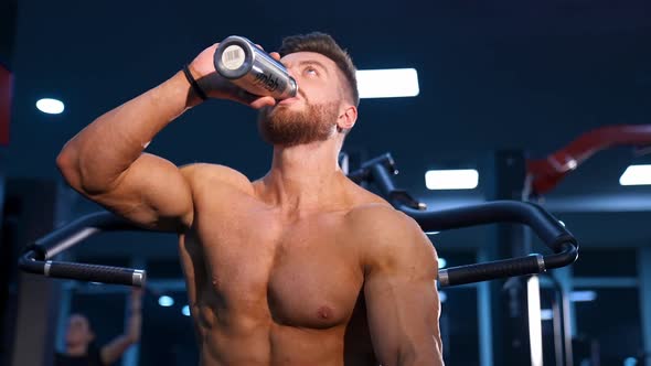 Man with perfect body train muscles on sport equipment and drinks water.