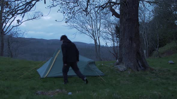 Young man camping alone walks past tent in wilderness