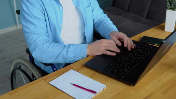 Male Student Learning Online Using Laptop Typing Sitting in Wheelchair in Apartment Busy with