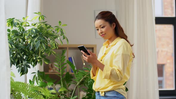 Asian Woman with Smartphone and Flowers at Home