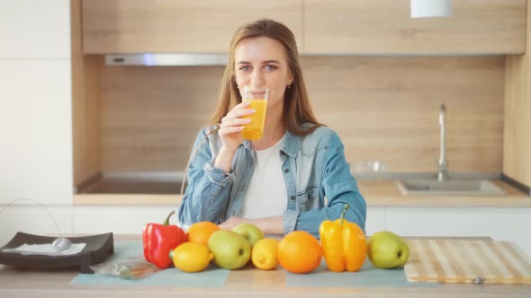 A Beautiful Young Woman with Glass of Juice Is Sitting at Kitchen Table