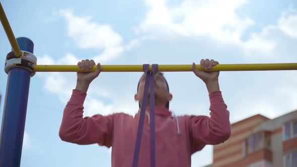 A Young Man Performs Pullup Exercises with Fitness Elastic Bands on the Street