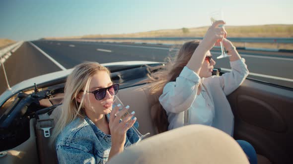 Two Women in Summer Clothes and Sunglasses Driving in Convertible Drink Champagne and Enjoy Life
