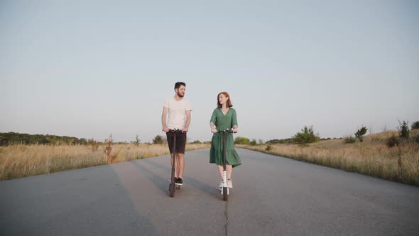 Couple in Love Riding on Electric Scooters to the Camera on the Way Out of Town