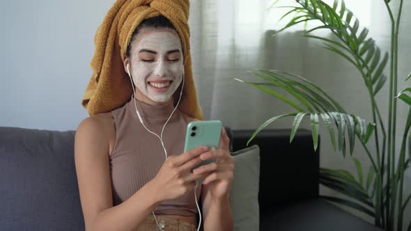 Young woman using mobile smartphone while having skin care spa day at home