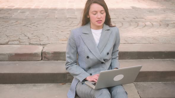 Young Woman Sitting on Stairs While Has Video Call Chatting on Laptop on the Street