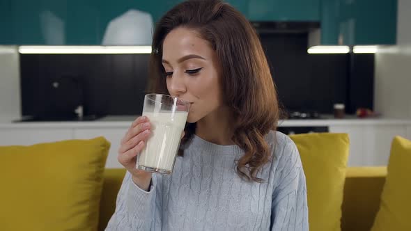 Young Woman Drinking a Glass of Milk, Sitting on the Comfortable Couch in the Kitchen