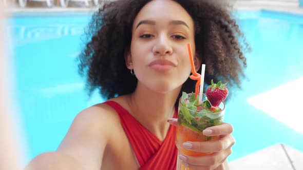 Young Girl Teenager Internet Vlogger Poses in Front of Camera with Cocktail in Pool, Folds Bow Her