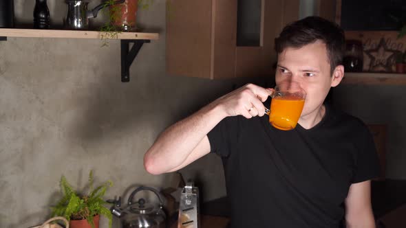 A man drinks orange juice in the kitchen. 
