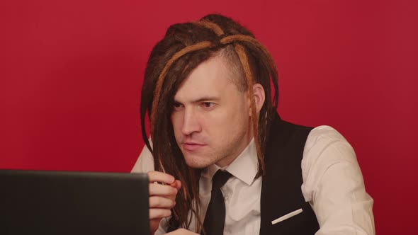 Young Man in Business Suit Works on Laptop and Eats Nuts Sitting in Home Office