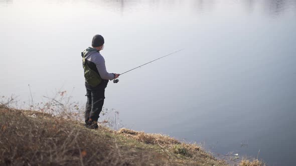 Footage of a Man Wearing a Backpack Using a Fishing Rod Trying to Catch Fish