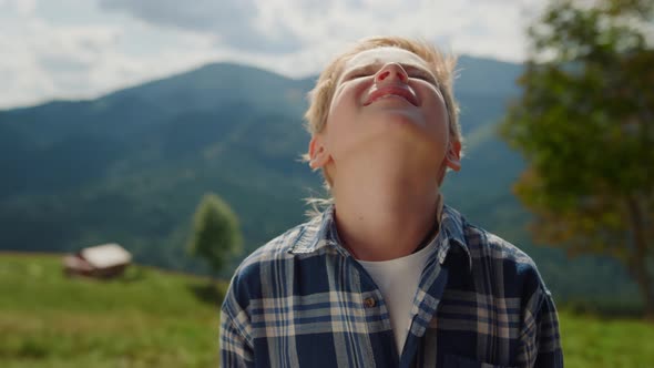 Little Boy Enjoying Sunlight Raising Head to Sky in Summer Mountains Close Up