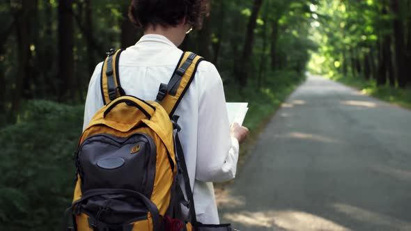 A Girl Tourist With A Bright Backpack Moves, Holding A Travel Map In Her Hands, Tourist Route