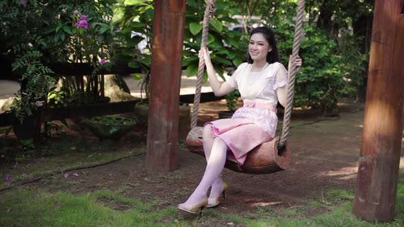 slow-motion of happy young woman in Thai traditional dress relaxing on a wooden swing