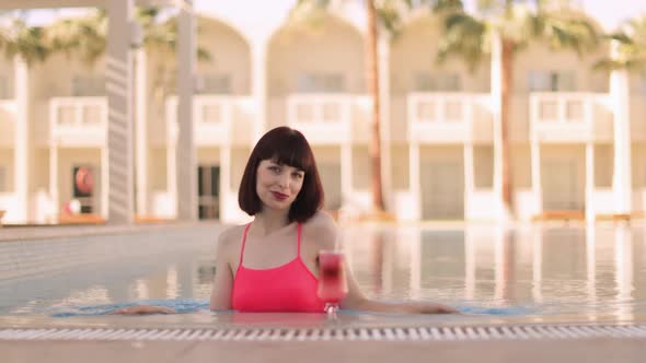 Pretty Young Lady with Drink in Pool Enjoying Summer Vacations