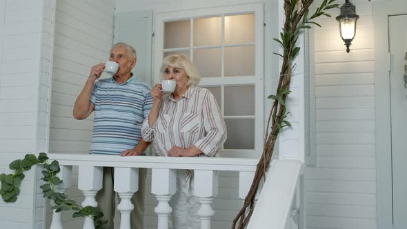 Senior Elderly Caucasian Couple Drinking Coffee, Embracing in Porch at Home. Mature Happy Family