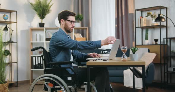 Handicapped Man in Wheelchair Working on Laptop in Home Office at daytime