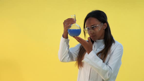 Pretty Black Woman in Safety Glasses and Lab Coat Holding Flask with Liquid in Her Hands