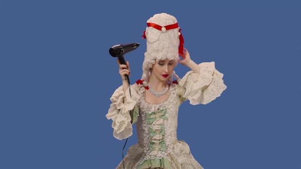 Portrait of Courtier Lady in White Vintage Lace Dress and Wig is Dries Hair with a Hair Dryer