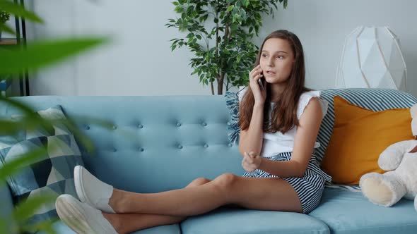 Carefree Teenage Girl Chatting on Mobile Phone Sitting on Comfy Couch at Home