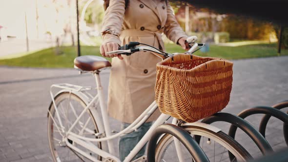 Unknown Female is Leaving Her Cruiser Bike on a Steel Parking Rack of a City Park and Go Away