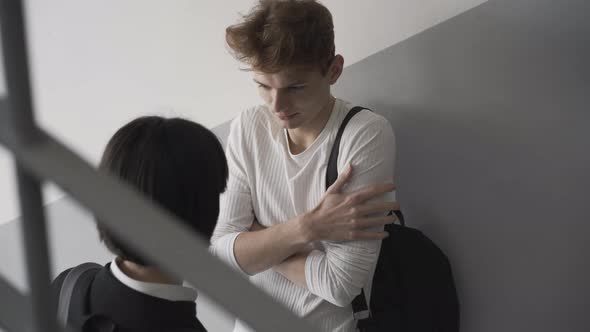 Closeup of Shy High School Student Standing at Wall on Stairs As Confident Girl Kissing Boy on Cheek