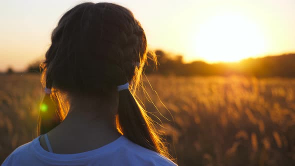 Dolly Shot of Cute Small Girl Stands at Grass Meadow Looking at Beautiful Evening Sunset